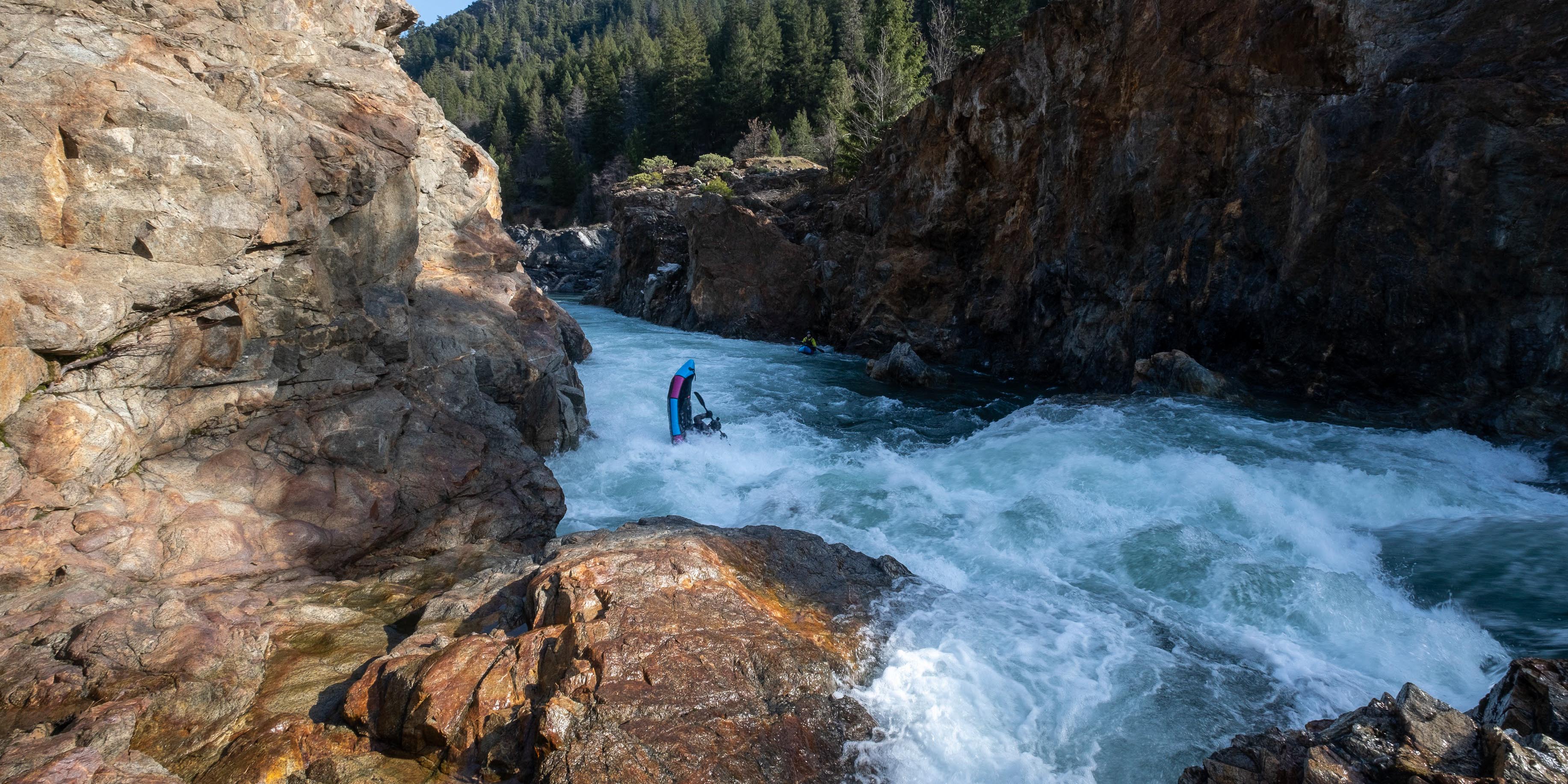 Person pack rafting through a narrow river gorge with rocky walls and water rapids.